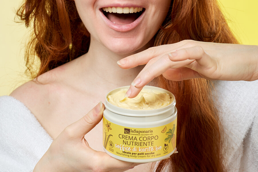 Crema-corpo-biologica-nutriente-soffice-di-karitè-bio-ambientata-ragazza-mano-sorriso-capelli sciolti